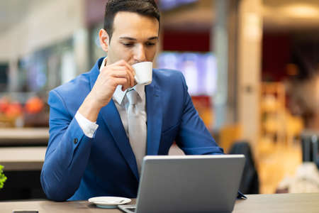 Young businessman drinking a coffee while working at his laptopの写真素材