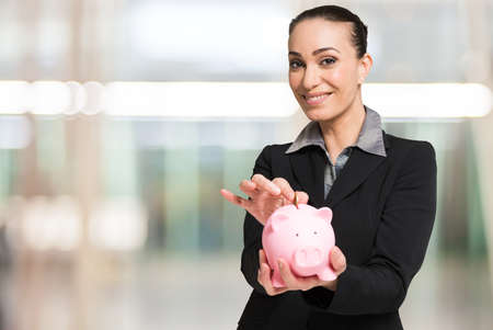 Woman putting a coin in her piggy bank. Saving and money spare conceptの写真素材
