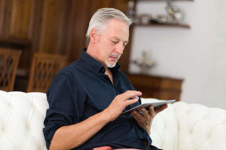 Portrait of a smiling senior man using a digital tablet in the living room of his apartment