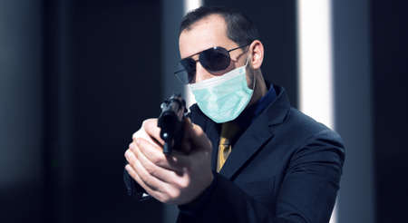 Secret agent holding a gun while wearing a mask, coronavirus and pandemic concept