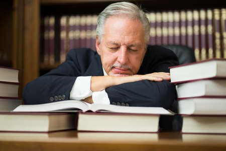 Sleepy business man lawyer surrounded by many booksの写真素材
