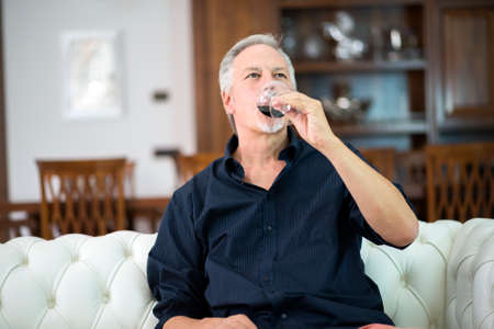Portrait of a mature man enjoying a glass of red wine at homeの写真素材