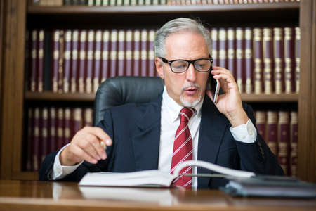 Businessman reading a book while talking on his mobile phoneの写真素材