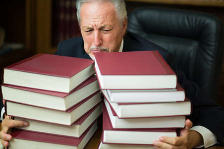 Tired and stressed business man lawyer surrounded by many booksの写真素材