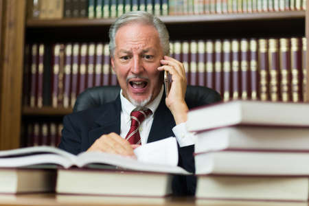Angry businessman yelling on the cellphone while reading a bookの写真素材
