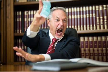 Angry business man thowing away a surgical maskの写真素材