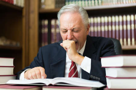 Sleepy business man lawyer yawning. Surrounded by many booksの写真素材
