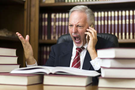 Angry businessman yelling on the cellphone while reading a bookの写真素材