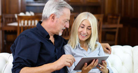 Portrait of a smiling mature couple using digital tablet on sofa at homeの写真素材