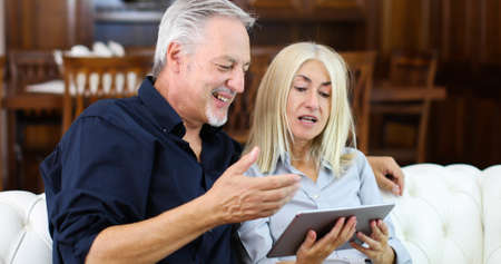 Portrait of a smiling mature couple using digital tablet on sofa at homeの写真素材
