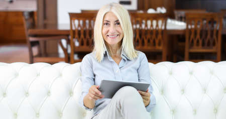 Beautiful mature woman using electronic tablet at homeの写真素材