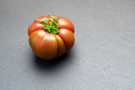 Closeup shot of a tomato lying on a dark surfaceの写真素材