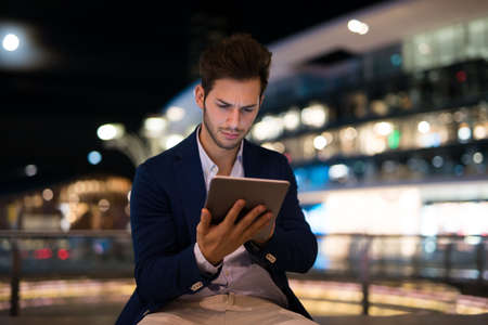 Portrait of man using his tablet in a city at nightの写真素材