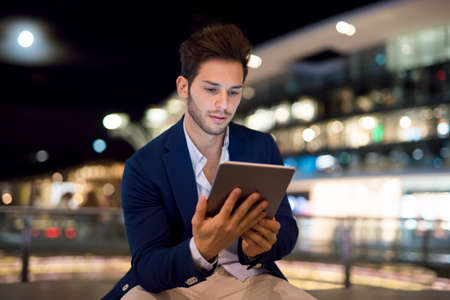 Portrait of man using his tablet in a city at nightの写真素材