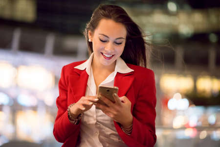 Business woman using her cell phone at night outdoors in a big cityの写真素材