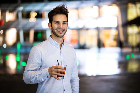 Young man holding a drink at a night club outdoorの写真素材