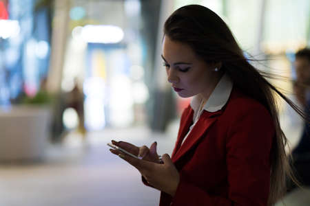 Woman using her smatphone outdoor in the evening in a modern city settingの写真素材