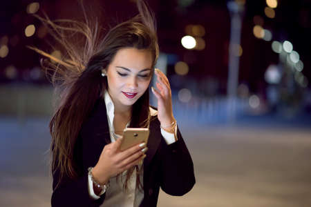 Woman using her cellphone at night in a cityの写真素材