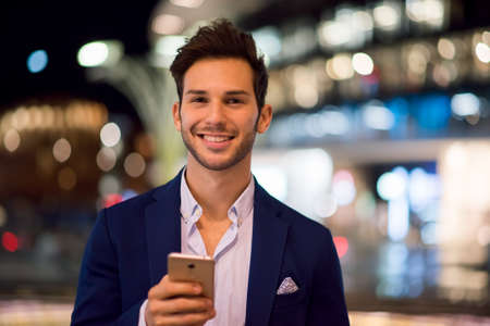 Young man using his cellphone while walking at nightの写真素材