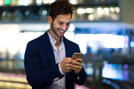 Young manager using his smartphone outdoor at night in the cityの写真素材