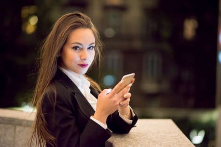 Woman using her cellphone at night in a cityの写真素材