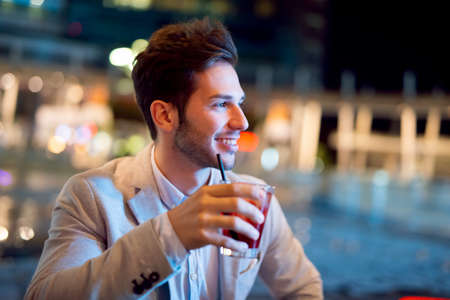 Young man holding a drink at a night club outdoorの写真素材
