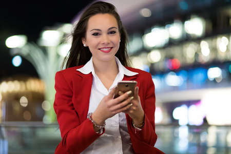 Woman using her smatphone outdoor in the evening in a modern city settingの写真素材