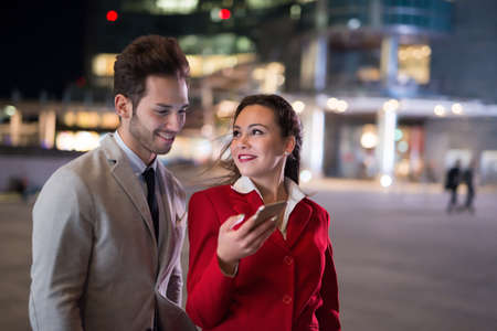 Business people businessman and businesswoman using a smartphone at night in a cityの写真素材