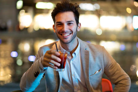 Young man holding a drink at a night club outdoorの写真素材