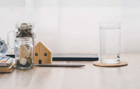 Wood house model, pen telephone coin and glass water on a tableの写真素材