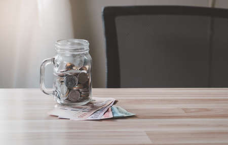 Thai bank notes and coins in glass jar on wood table background, business savings and salary account concept.の写真素材