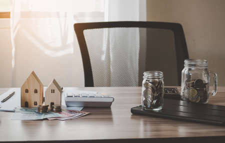 Image of wood house model calculator banknote and coins in glass on desk of working business people. office supplies in office room.の写真素材