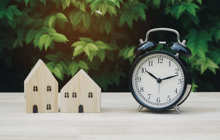 Wood house model and black o'clock on desk with green nature blur Background. Savings Plans for Housing. Finance and Banking about House concept.の写真素材