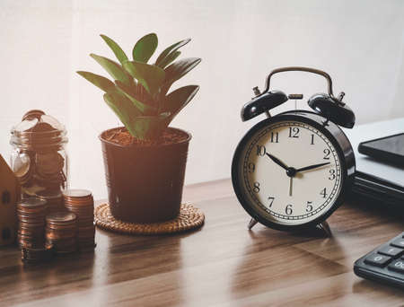 Image of black clock green tree stack coins and coins in glass on desk of working business people. office suppliesの写真素材