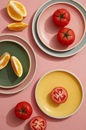Minimal flatlay of tomato and orange on pastel plates with linen napkin. Flat lay, top view.の写真素材
