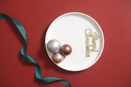On the red background, a white ceramic dish containing baubles and â€œMerry Christmas text...