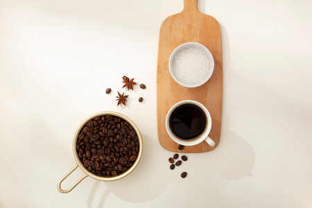 Against the white background, coffee beans on golden tray decorated with cup of coffee and bowl of bath salt on wooden cutting board. Natural ingredients for body skin careの写真素材