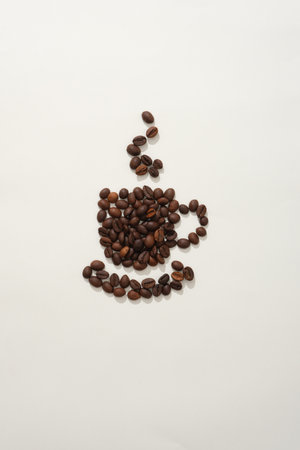 On the white background, brown roasted coffee beans arranged in the shape of a cup of coffee with hot smoke rising from it. Creative background for advertising. Top viewの写真素材
