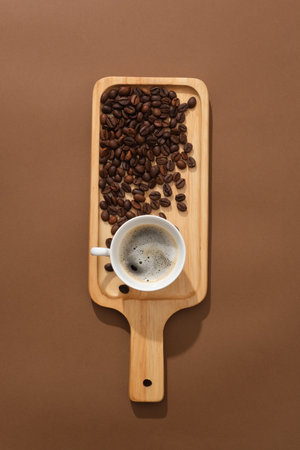 Against the brown background, a delicious cup of espresso decorated with coffee beans on wooden cutting board. Scene for advertising drinking product with minimal conceptの写真素材