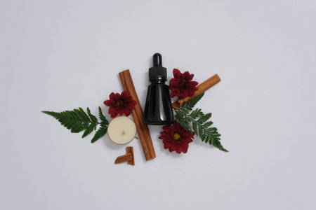 Blank amber glass essential oil bottle with red flower, fern leaves, cinnamon sticks and candle...