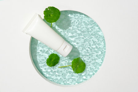 A glass platform features a cosmetic tube and pennywort leaves, creating a ripple effect. An empty...
