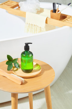 Close-up of a transparent green shampoo bottle placed on a ceramic plate, green leaves and a brush...