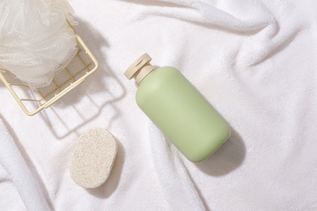 A bath sponge in an iron basket, a bar of soap and an unlabeled bottle of shower gel are displayed on a white fabric background. Minimalist space for advertising.の写真素材