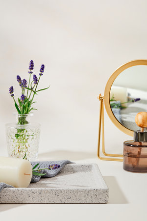 Lavender flowers inside a glass vase on a gray tray with candles and towels, and a diffuser of...