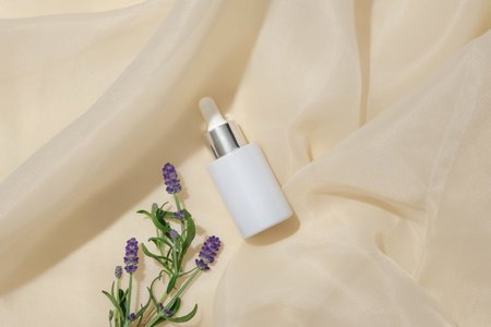 A bottle of white serum and fresh lavender flowers stand out on a beige fabric background. Blank labels for branding and advertising. Lavender essence has the effect of cleansing the skin.の写真素材