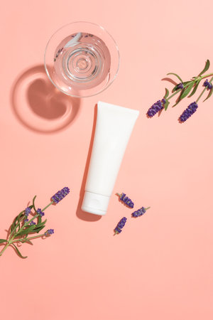 View from above of an unlabeled cosmetic tube, lavender flowers and a cocktail glass on a pink background. Cosmetic advertisement with lavender extract.の写真素材