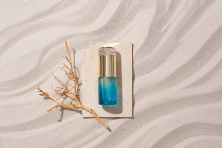 A dry branch and a cosmetic bottle are displayed on a stone platform on a sandy background with...