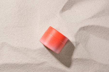 Close-up of a red cosmetic jar isolated on a beige sand background. Blank labels for branding. Copy...