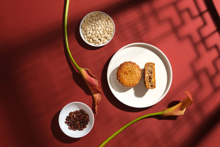 Against the red background, three white ceramic dishes filled with appetizing mooncakes, watermelon seeds and pumpkin seeds decorated with flowers. Scene for advertising. Chinese Mid-autumn festivalの写真素材