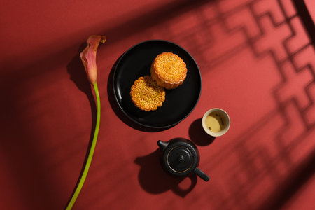 Creative layout for advertising mooncake product on mid-autumn festival. On a red background, delicious mooncakes on ceramic dish decorated with black tea set and beautiful flowerの写真素材